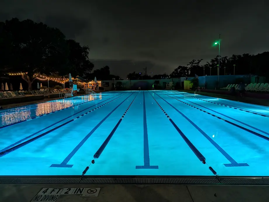 The lap lanes lit turquoise after dark, string lights along the far deck