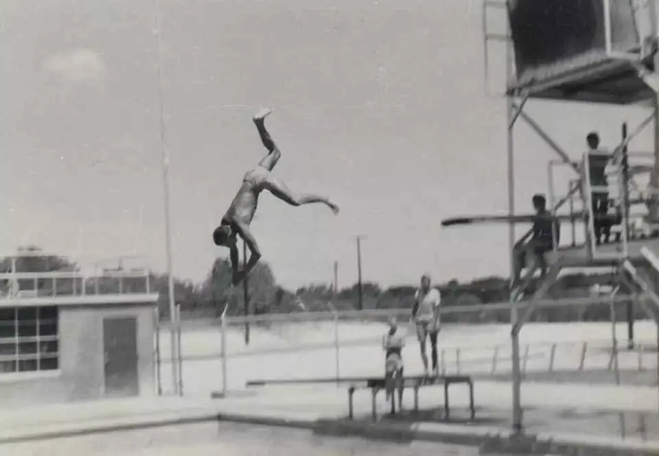 Black-and-white photograph of a swimmer mid-dive off the old high dive tower