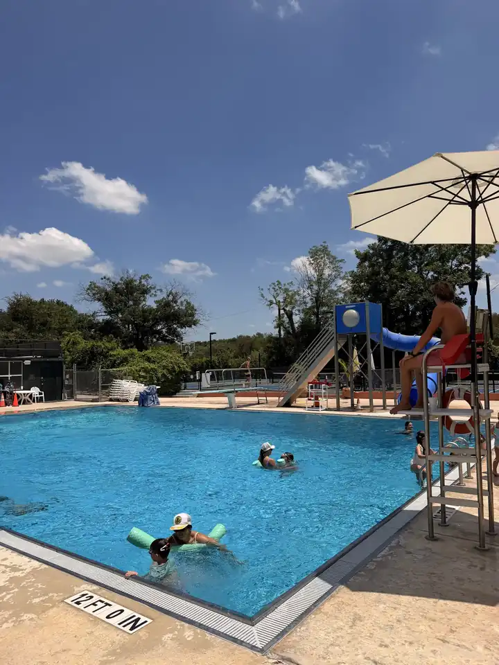 Diving well with the board, the tall slide tower and a lifeguard chair under a striped umbrella