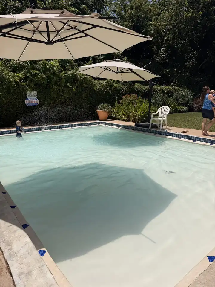 Shallow kiddie pool under two large umbrellas with lounge chairs along the edge