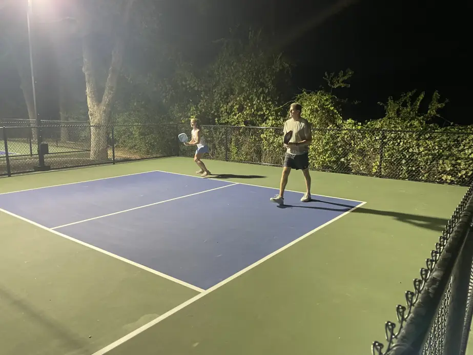 Two players on a lit blue-and-green pickleball court at night